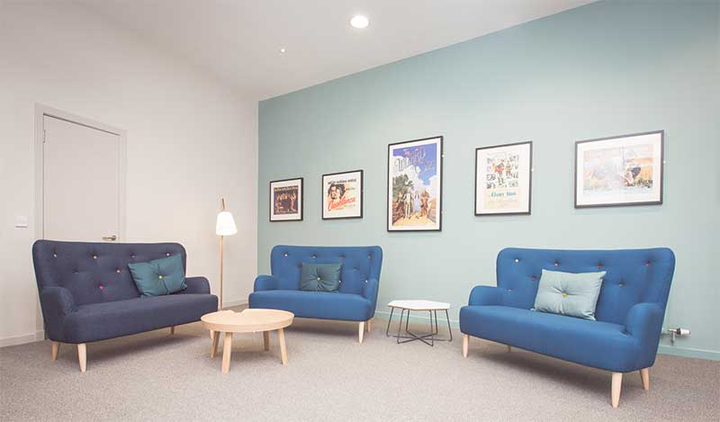 A blue couch and chair in a warmly decorated room with wall art, found in Alzheimer Scotland Bungalow, Bonnyrigg, Midlothian.